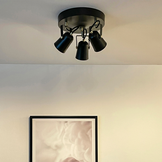 Interiørbilde av lysende Metz takspot med tre justerbare spotter på en rondell i sort metall og detaljer i messing - Aneta belysning