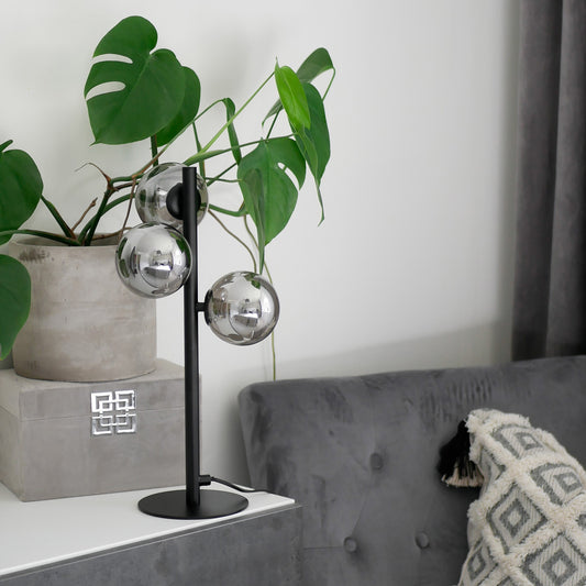 Molekyl bordlampe i en stue, laget i svart metall og tre sotede glasskupler festet langs lampefoten - Aneta belysning