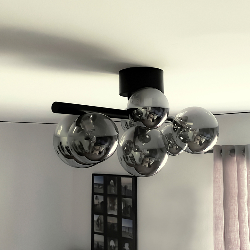 Molekyl taklampe plafond i en stue, laget i svart metall og med syv sotede glasskupler festet langs en rett stang - Aneta belysning