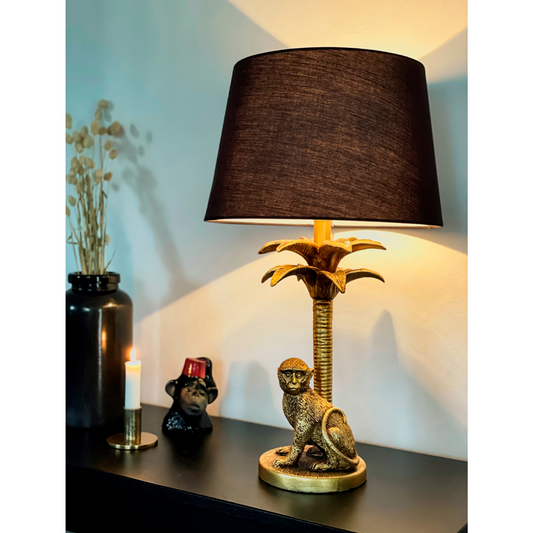 Interiørbilde av Markatta bordlampe med lampefot i gull formet som en marekatt og en palme, og lampeskjerm i sort tekstil - Aneta belysning
