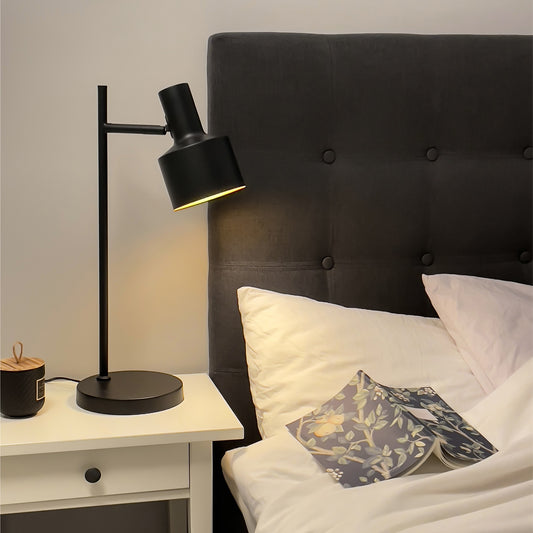 Ferdinand retroinspirert bordlampe lysende på et nattbord, laget i svart metall med gyllen innside av skjermen - Aneta belysning