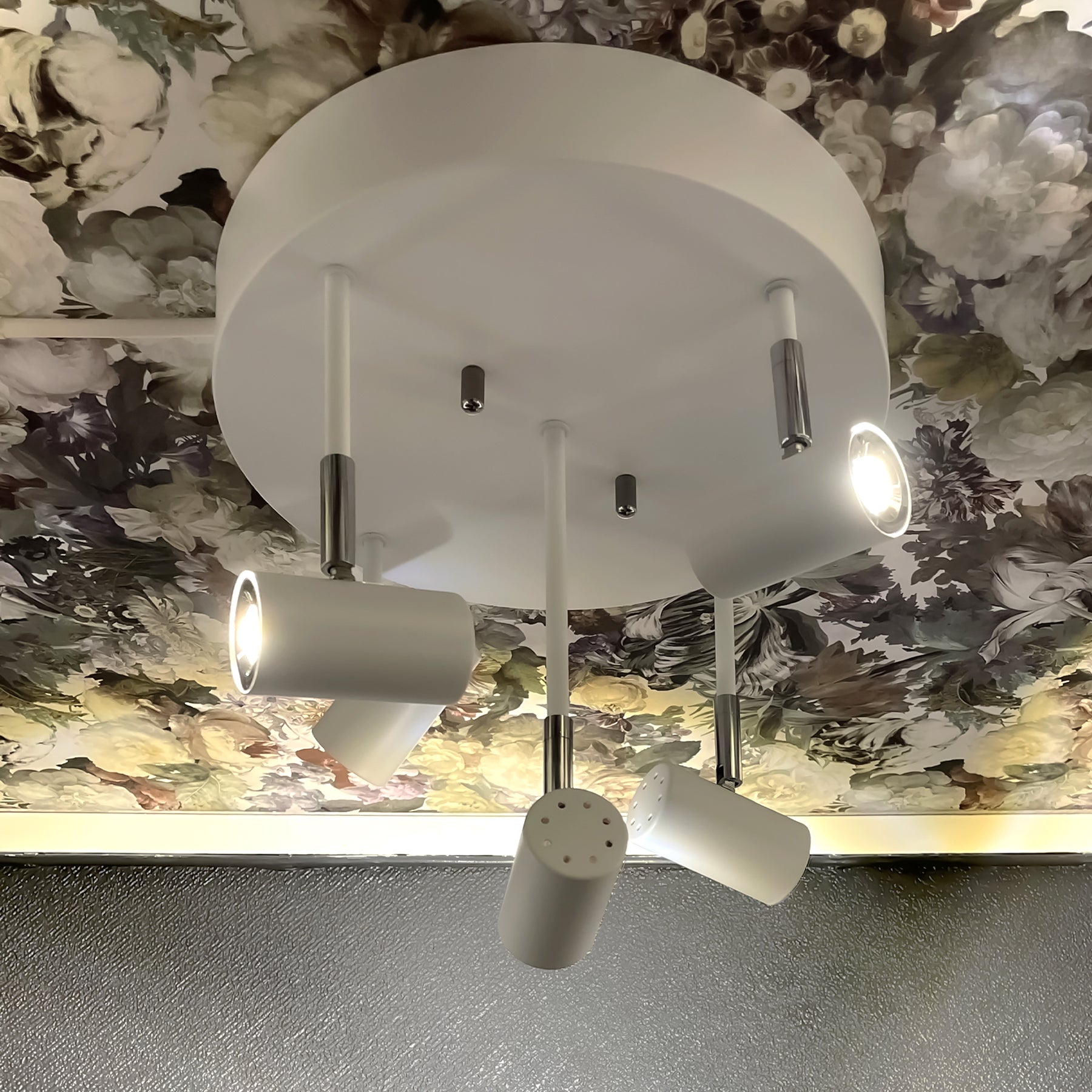 Lysende Gusto spotlight taklampe med fem justerbare spotter i ulik høyde plassert på en rund takplate, laget i hvit metall med detaljer i krom - Aneta belysning