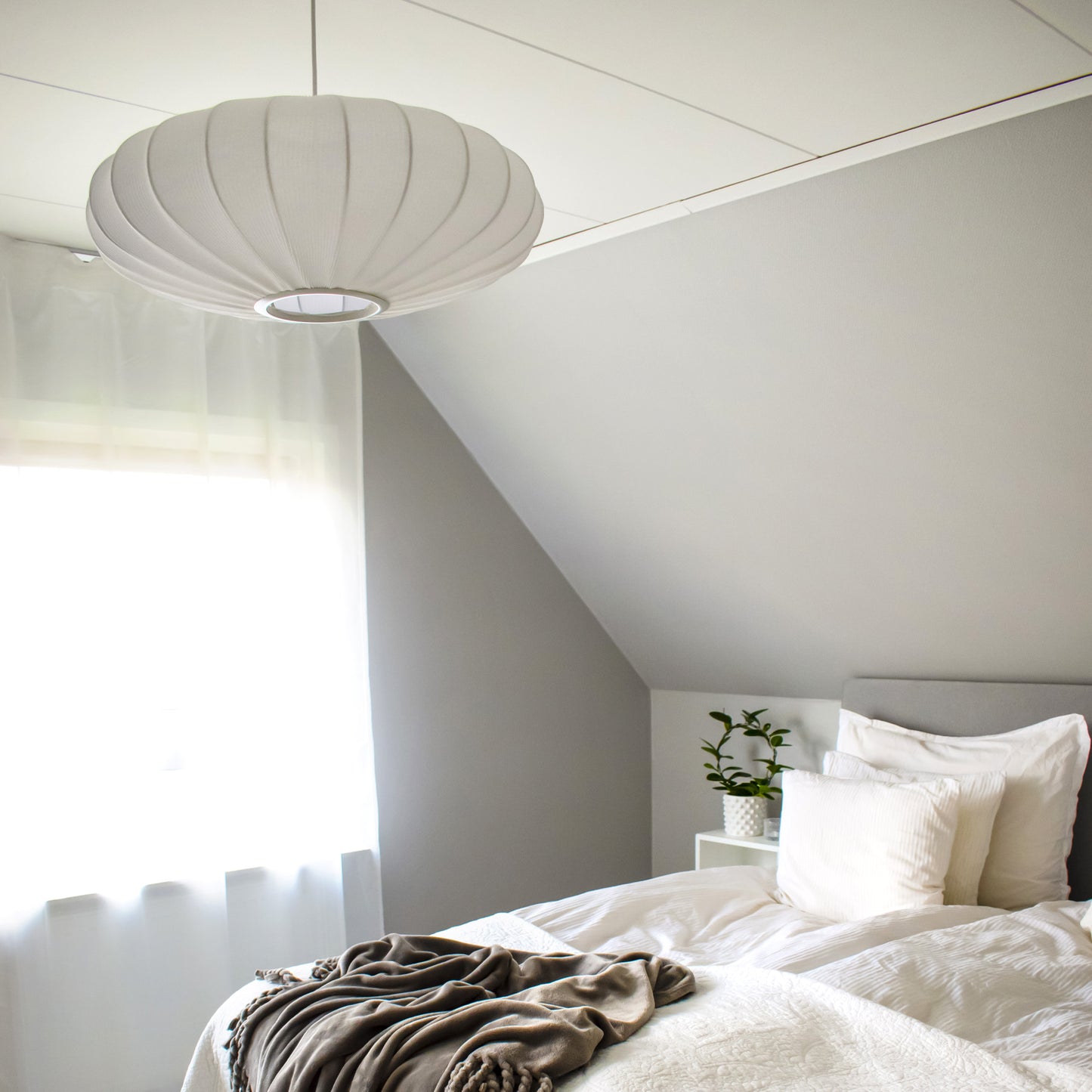 Mamsell taklampe hengende på et soverom, en rund pendel med diameter 55cm trukket i hvit tekstil rundt en ramme i hvit metall - Aneta belysning