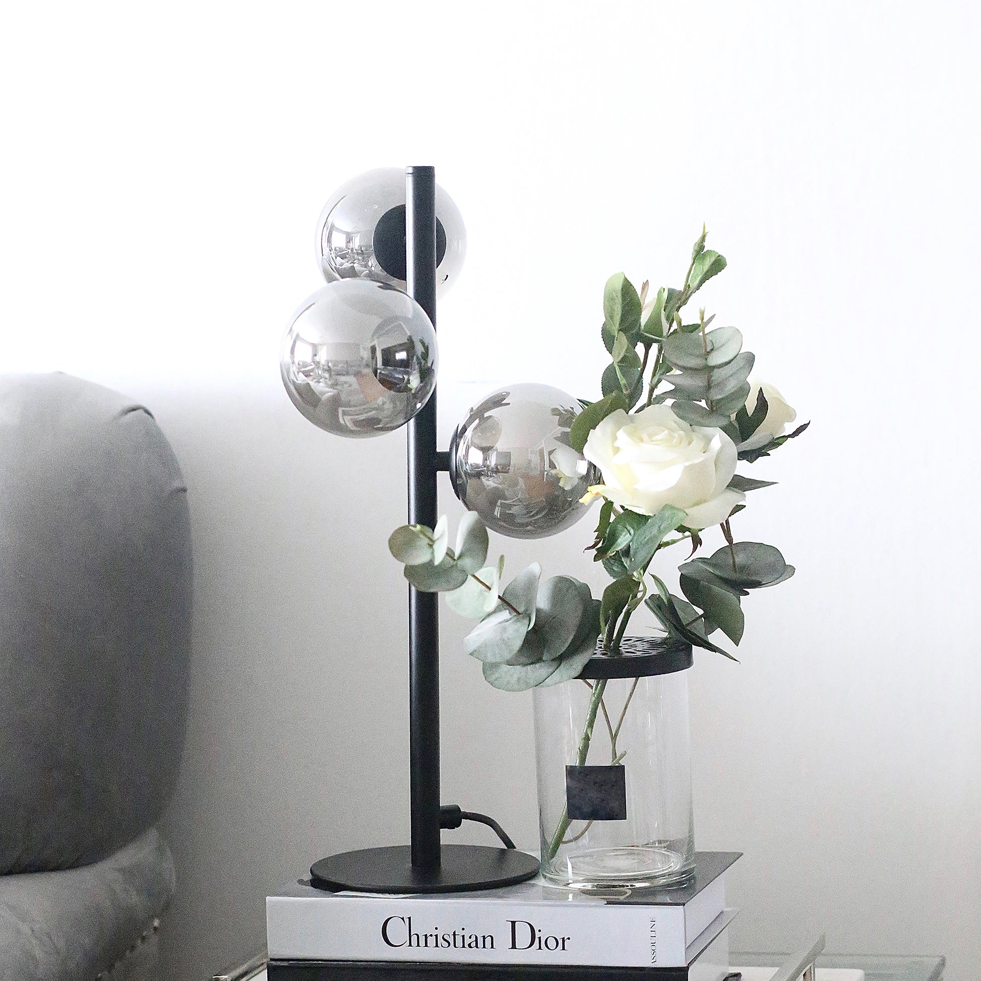 Molekyl bordlampe på et nattbord, laget i svart metall og tre sotede glasskupler festet langs lampefoten - Aneta belysning