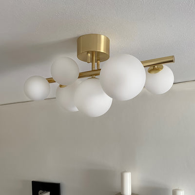 Molekyl taklampe plafond i en stue, laget i messing metall og med syv opale glasskupler festet langs en rett stang - Aneta belysning