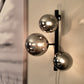 Molekyl vegglampe lysende i en stue, laget i sort metall og tre sotede glasskupler festet langs en loddrett stang - Aneta belysning